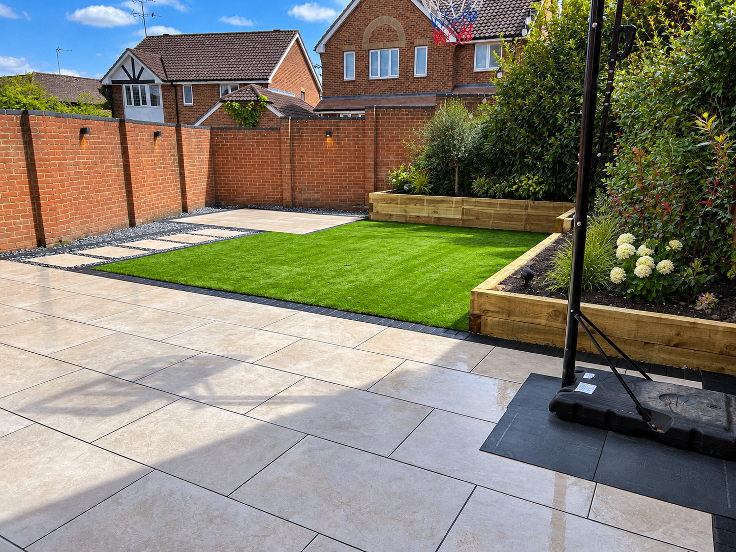 Light-paved driveway beside artificial turf, a brick boundary wall and raised timber beds